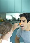 Girl holding up cherry tomato to man's nose