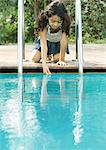 Girl crouching by edge of pool, touching surface of water