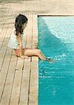 Girl sitting on edge of pool, dangling feet in water