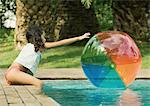 Girl sitting on edge of pool, reaching for beach ball in water
