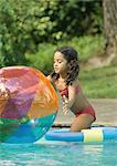 Girl standing in pool, reaching for beach ball