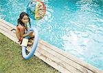 Fille assise en bord de piscine, tenant l'anneau flottant