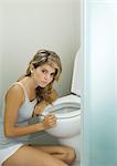 Young woman sitting on floor, leaning against toilet bowl