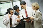 Four business colleagues standing looking at document while one uses phone