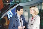 Male and female business associates standing in lobby, talking and smiling