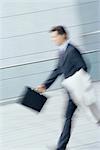 Businessman walking with briefcase and jacket over arm, blurred motion