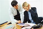 Business colleagues, man leaning over woman's shoulder, pointing to documents