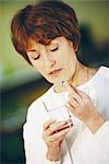 Senior woman taking pill, holding glass of water