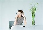 Woman using cell phone, holding pen and looking down at pad of paper