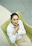 Businesswoman sitting in armchair, holding cell phone