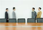 Business executives standing, facing associates arriving in conference room