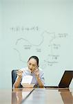 Businesswoman sitting at desk eating takeout food and using cell phone