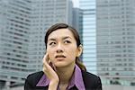 Businesswoman holding head and looking away, high rises in background