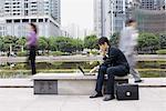 Businessman using laptop in office park, passers-by blurred in background