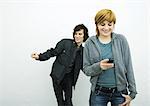 Young woman holding cell phone while young man behind her dances, white background