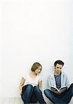 Teenage girl and young man sitting on floor with books, girl looking over at man's book