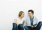 Teenage girl and young man sitting on floor with books, smiling at each other