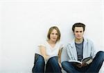 Teenage girl and young man sitting on floor with books, looking at camera