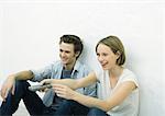 Teenage girl and young man sitting on floor, girl pointing remote control out of frame
