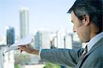 Businessman holding out paper airplane, skyline in background