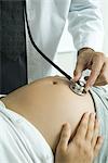 Doctor listening to pregnant woman's stomach with stethoscope