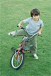 Boy getting on bike, on grass, high angle view, full length