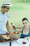 Woman taking kebab from tray of grilled meats, smiling at camera