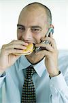 Man eating hamburger and using cell phone