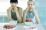 Woman and girl sitting side by side eating bowls of candy