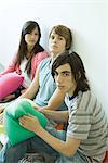 Three teen friends sitting on floor, holding cushions