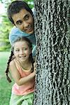 Girl and father peeking around tree