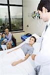 Boy lying in hospital bed surrounded by family and doctor