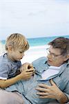Famille ayant un pique-nique sur la plage, garçon parler à grand-père