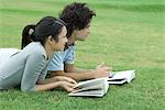 Young couple lying on grass with books, looking out of frame