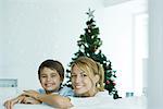 Boy and mother on sofa, Christmas tree in background, smiling at camera