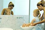 Femme aider petit lavage fille les mains dans l'évier de salle de bains