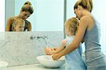 Woman helping little girl wash hands in bathroom sink