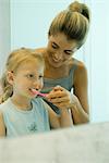 Woman helping little girl brush teeth