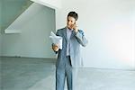 Well-dressed man looking at blueprints, using phone