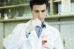 Young male scientist dipping microscope slide into solution in test tube
