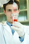 Young male scientist dipping microscope slide into solution in test tube, holding up slide