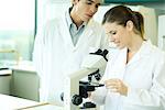Female lab worker placing slide under microscope, male colleague looking over shoulder