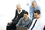 Four business associates looking at laptop computer together, smiling