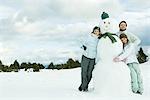 Trois jeunes amis s'appuyant sur le bonhomme de neige, souriant à la caméra, portrait