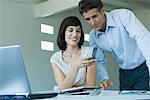 Young businesswoman holding up cell phone to mature male colleague, smiling