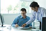 Two young businessmen looking at document together, laughing