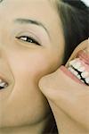 Cropped view of two young friends laughing together, one looking at camera, extreme close-up
