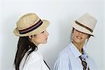 Two young female friends wearing hats and ties, looking at each other, one's eyes covered