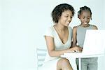 Mère et fille ensemble à l'aide d'ordinateur portable, en souriant, en regardant vers le bas