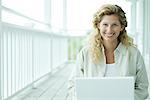 Woman using laptop computer on porch, smiling at camera, portrait